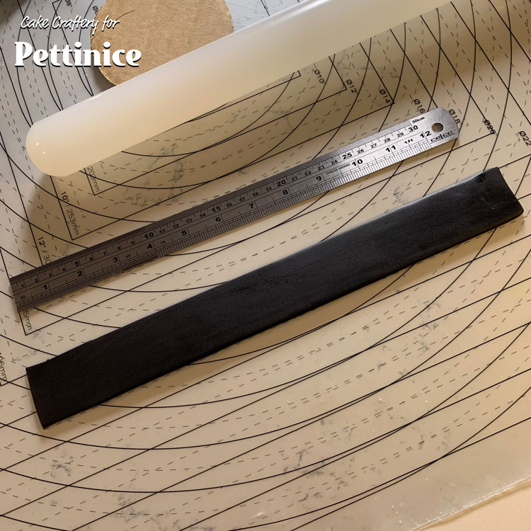 Now make the jacket collar. Start with a strip of black fondant that’s longer than you need - cut a strip that’s 3.5cm wide and about 35cm long. Make a stitch line on the top edge.