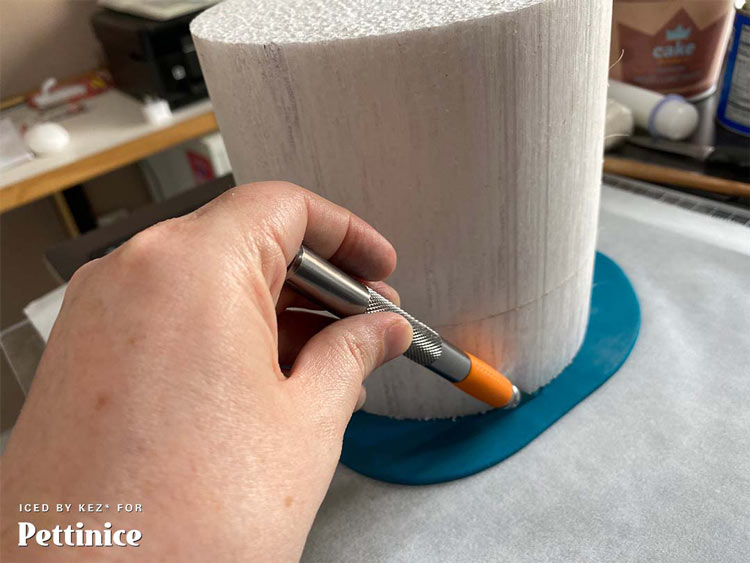 Take your xacto knife or a sharp blade and carefully cut around the cake - remove the excess fondant then take a flexible fondant smoother and smooth the edge of the fondant around the cake.